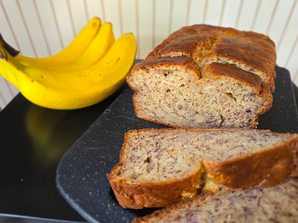 Golden-brown banana bread loaf with moist crumb structure, sliced to show tender interior, on a light surface