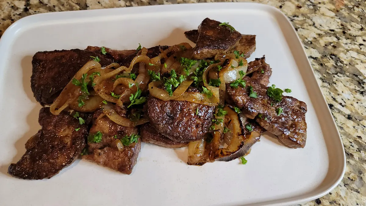 Pan-fried liver and onions on a white plate with golden caramelized onions and fresh herbs