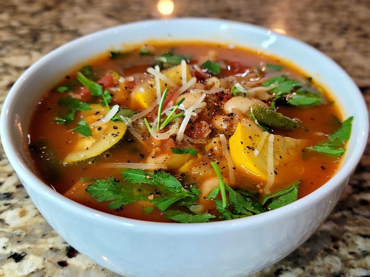 Bowl of hearty minestrone soup with colorful vegetables, olive oil drizzle, and fresh herbs on rustic table
