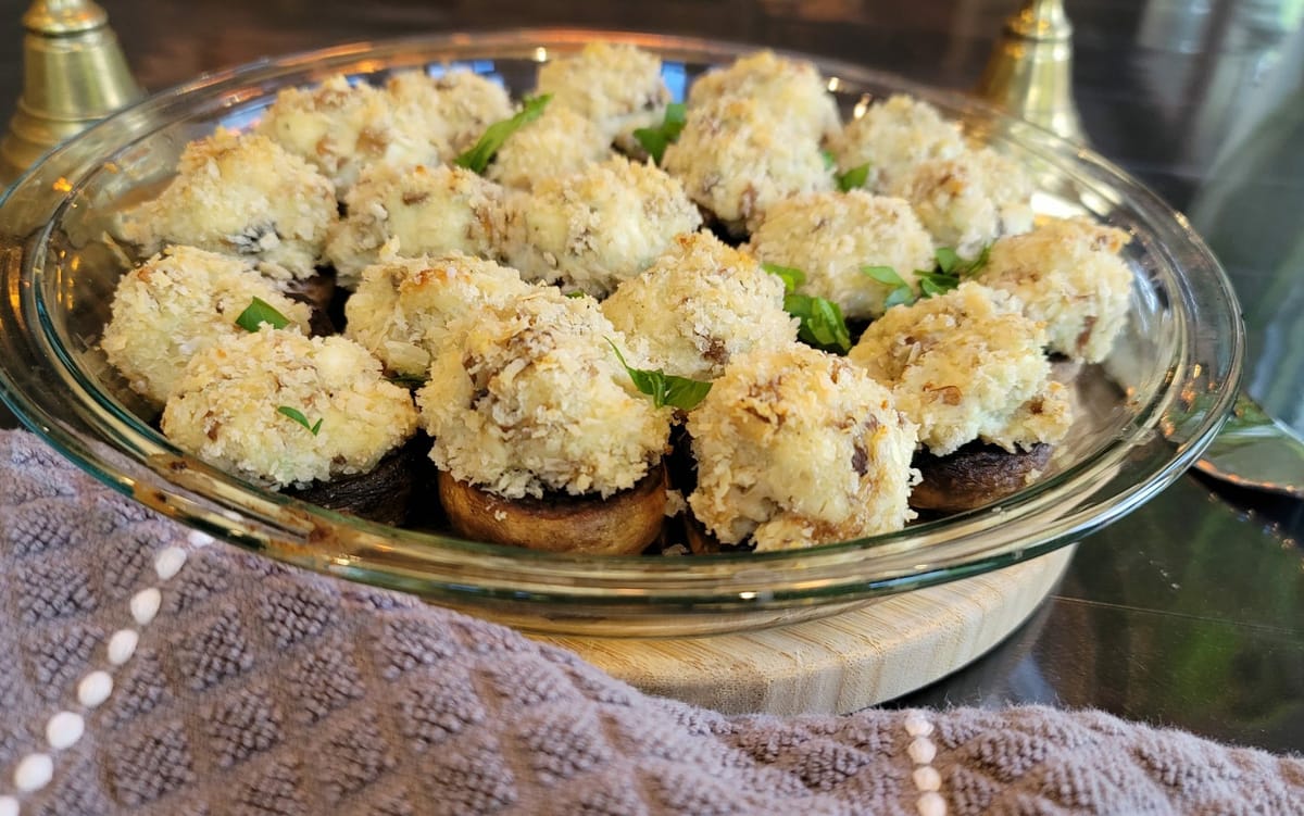 Golden baked stuffed mushrooms with cream cheese and Parmesan filling on a white plate, garnished with fresh herbs