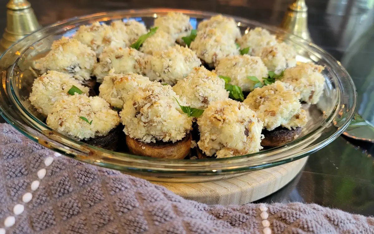 Golden baked stuffed mushrooms with cream cheese and Parmesan filling on a white plate, garnished with fresh herbs