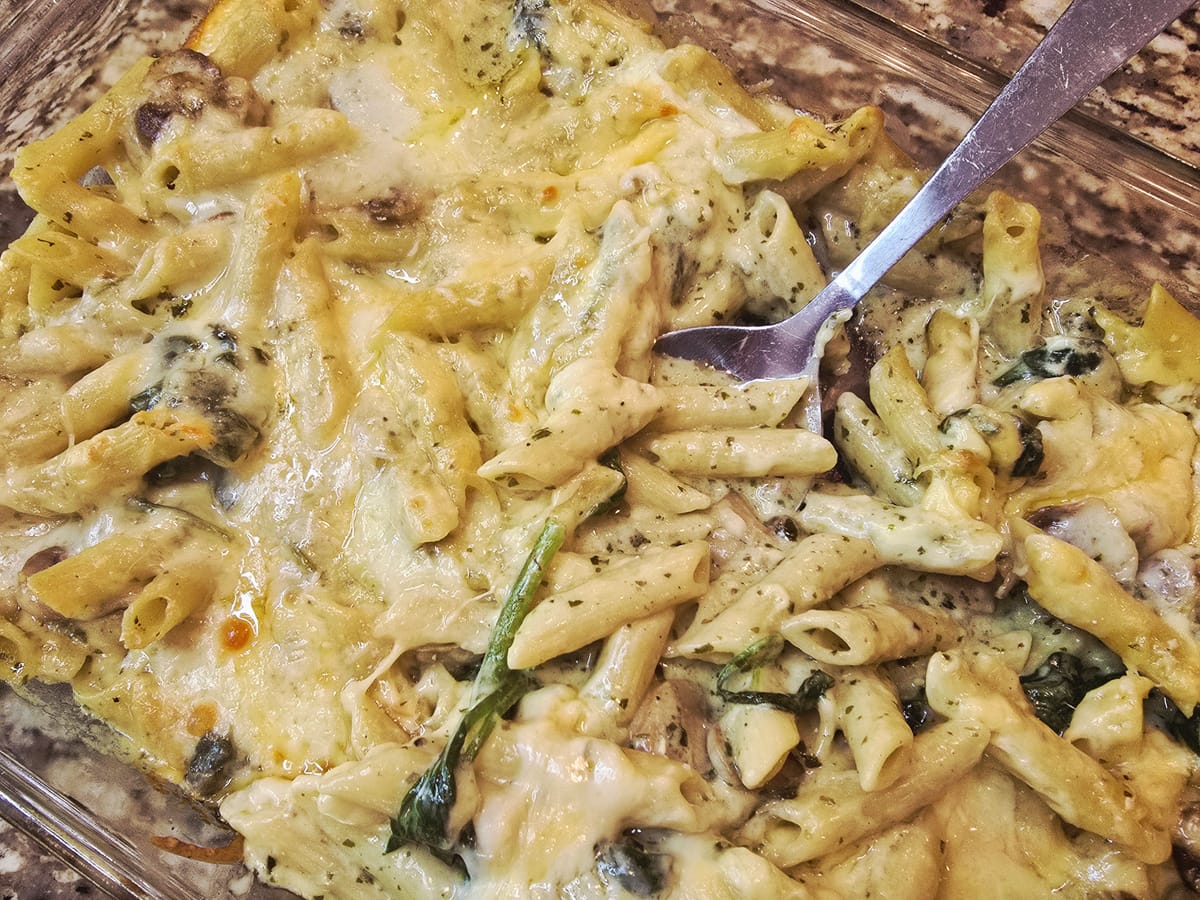Creamy mushroom spinach pasta bake with melted cheese topping in a white baking dish, topped with fresh herbs