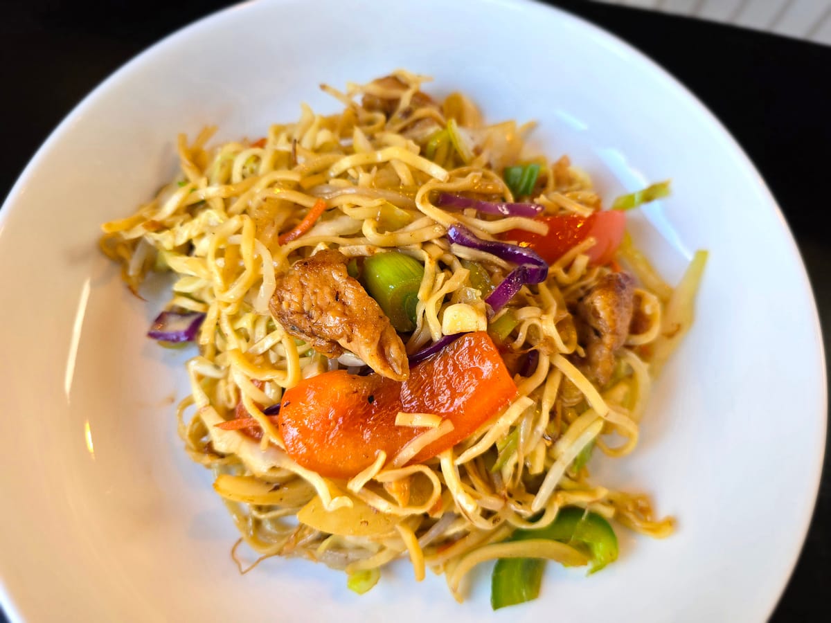 Golden crispy-bottomed chicken chow mein with fresh vegetables on a plate, garnished with green onions