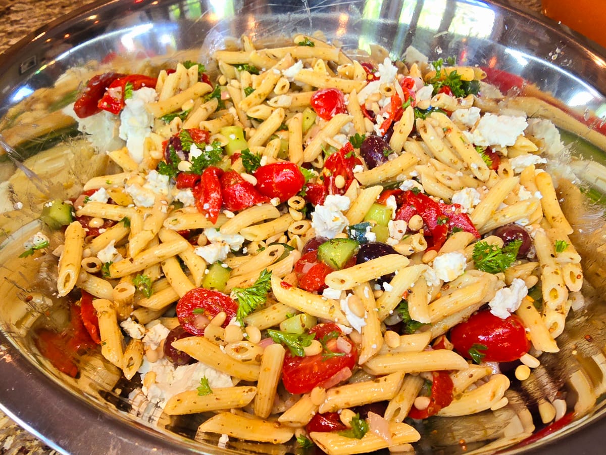 Colorful pasta salad with roasted red peppers, goat cheese crumbles, and fresh herbs in a white serving bowl