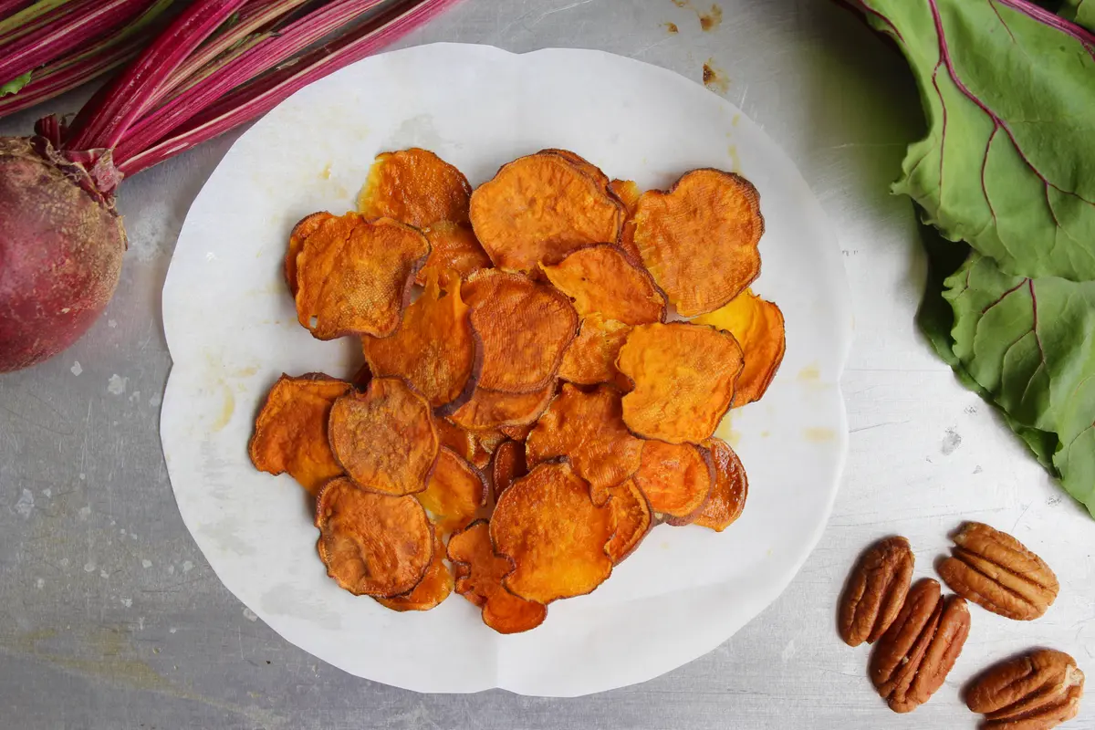Golden crispy oven-baked sweet potato chips arranged on parchment paper with a light dusting of seasoning
