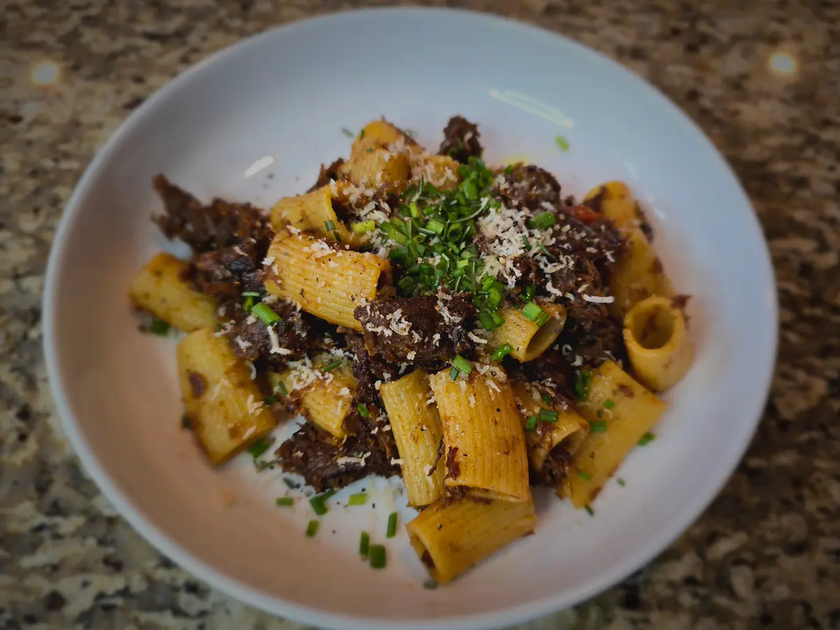 Bowl of pasta alla genovese with tender beef ragù, caramelized onions, and fresh parmesan on white plate