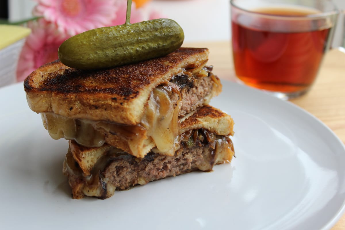 Golden crispy patty melt sandwich with melted cheese and caramelized onions, sliced in half on a plate