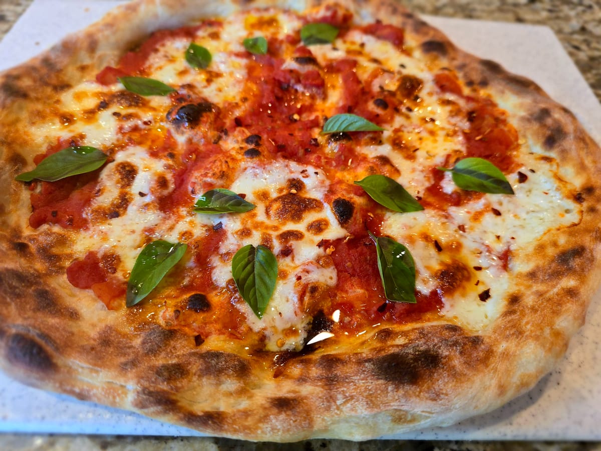 Golden-baked Pizza Margherita with melted fresh mozzarella, vibrant red San Marzano tomato sauce, and fresh basil leaves on a rustic surface