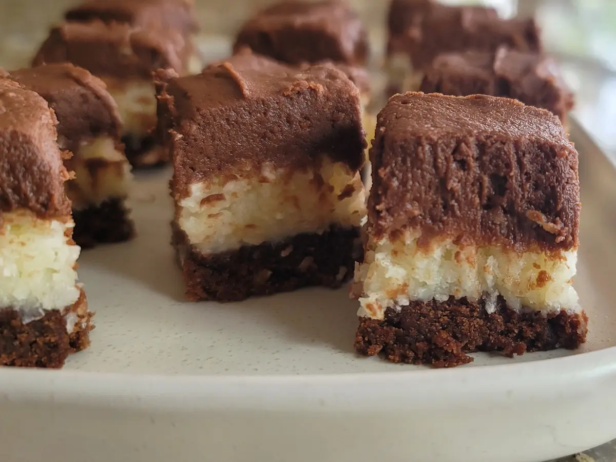 Queen Anne Squares stacked on a white plate, showing rich chocolate base layer and white coconut topping with smooth icing