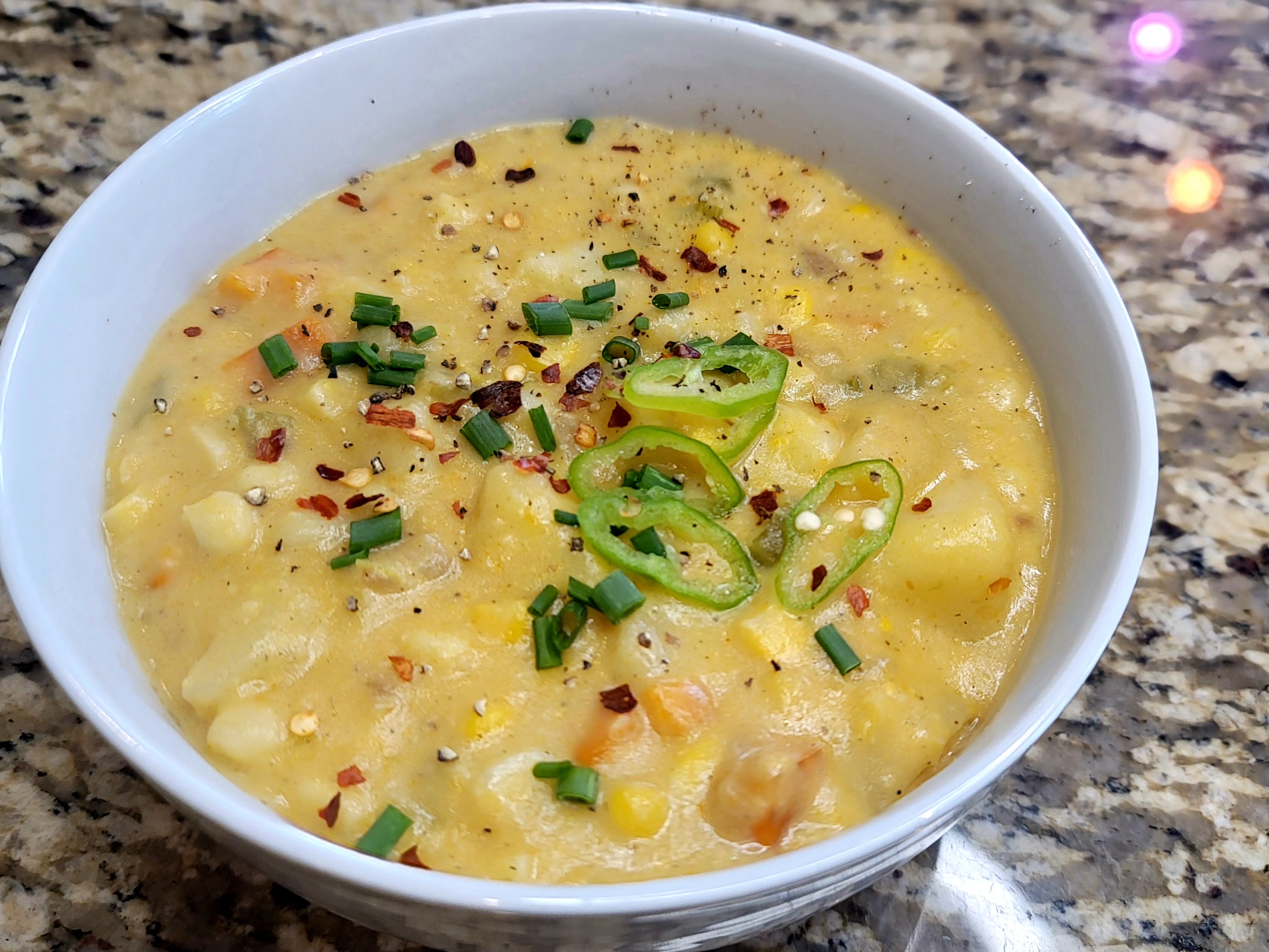 Creamy corn chowder in a white bowl garnished with fresh herbs and diced vegetables