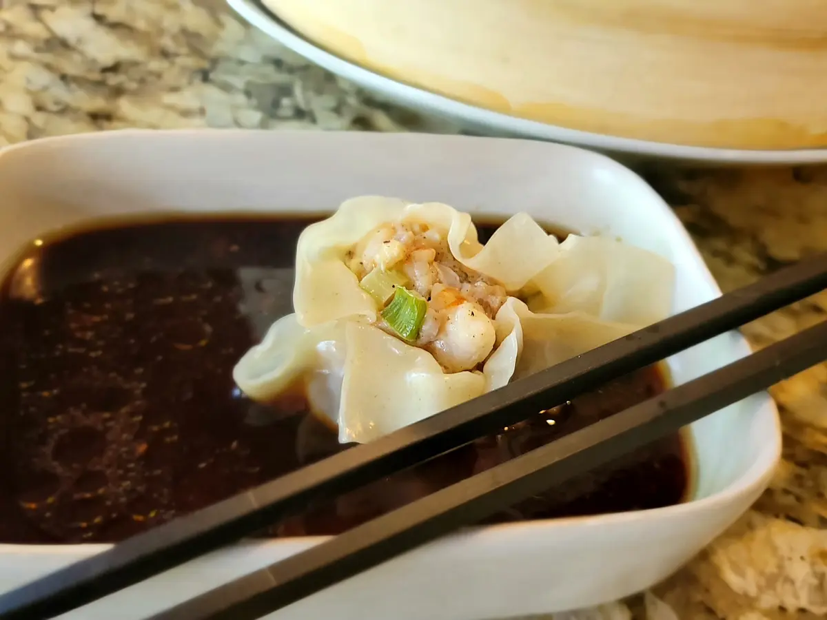 Homemade shrimp and pork dumplings on a white plate with soy dipping sauce and green onions