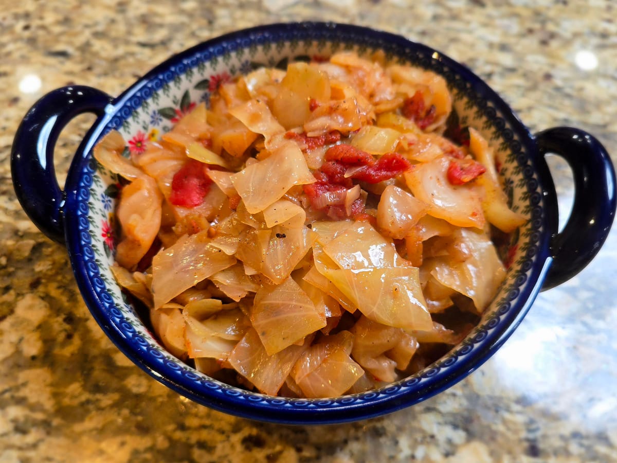 A bowl of tender stewed cabbage with tomatoes, onions, and garlic in a rich sauce, garnished with fresh herbs