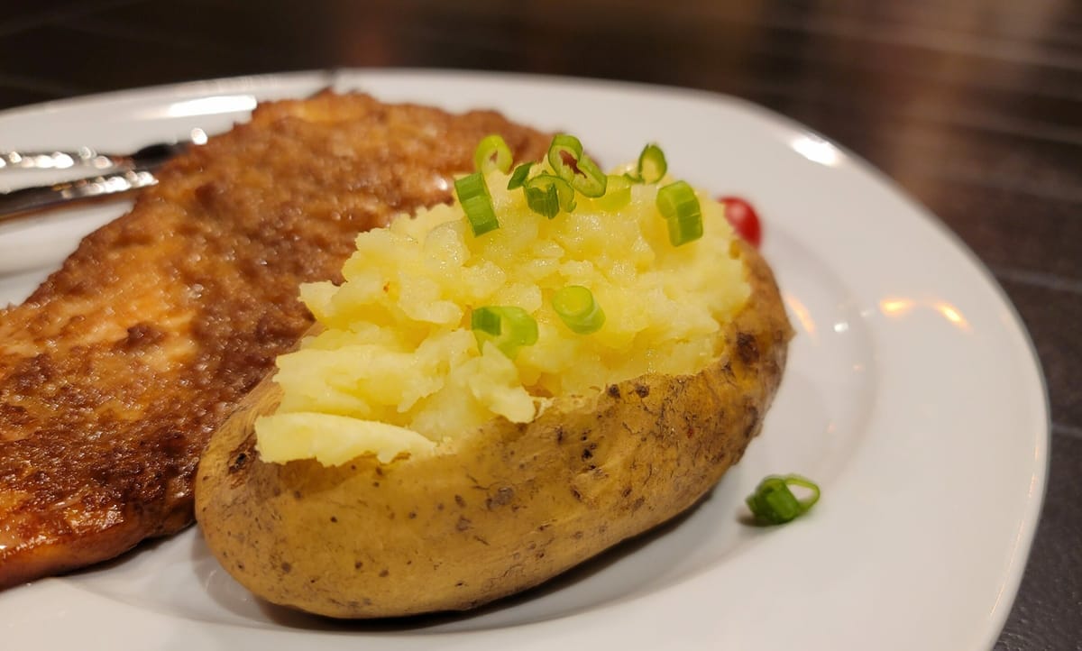 Fluffy baked potato halves stuffed with mashed potato, melted butter, and topped with grated cheese and green onions on a white plate