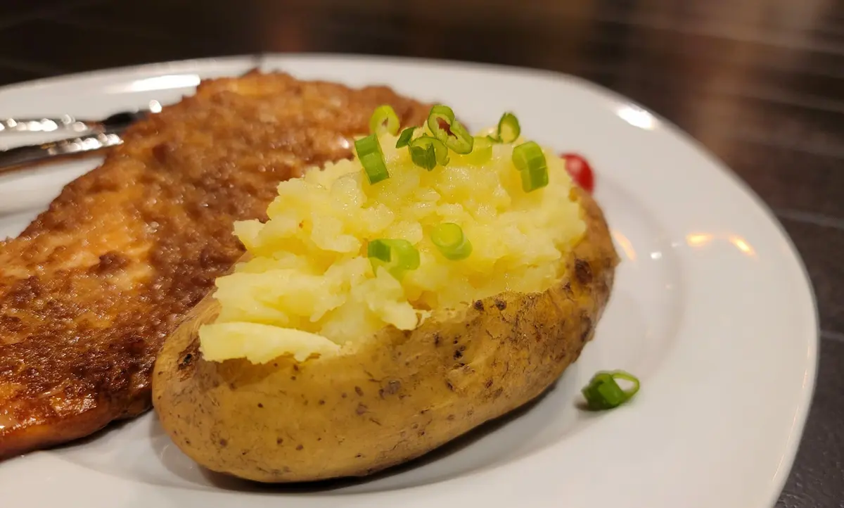 Fluffy baked potato halves stuffed with mashed potato, melted butter, and topped with grated cheese and green onions on a white plate
