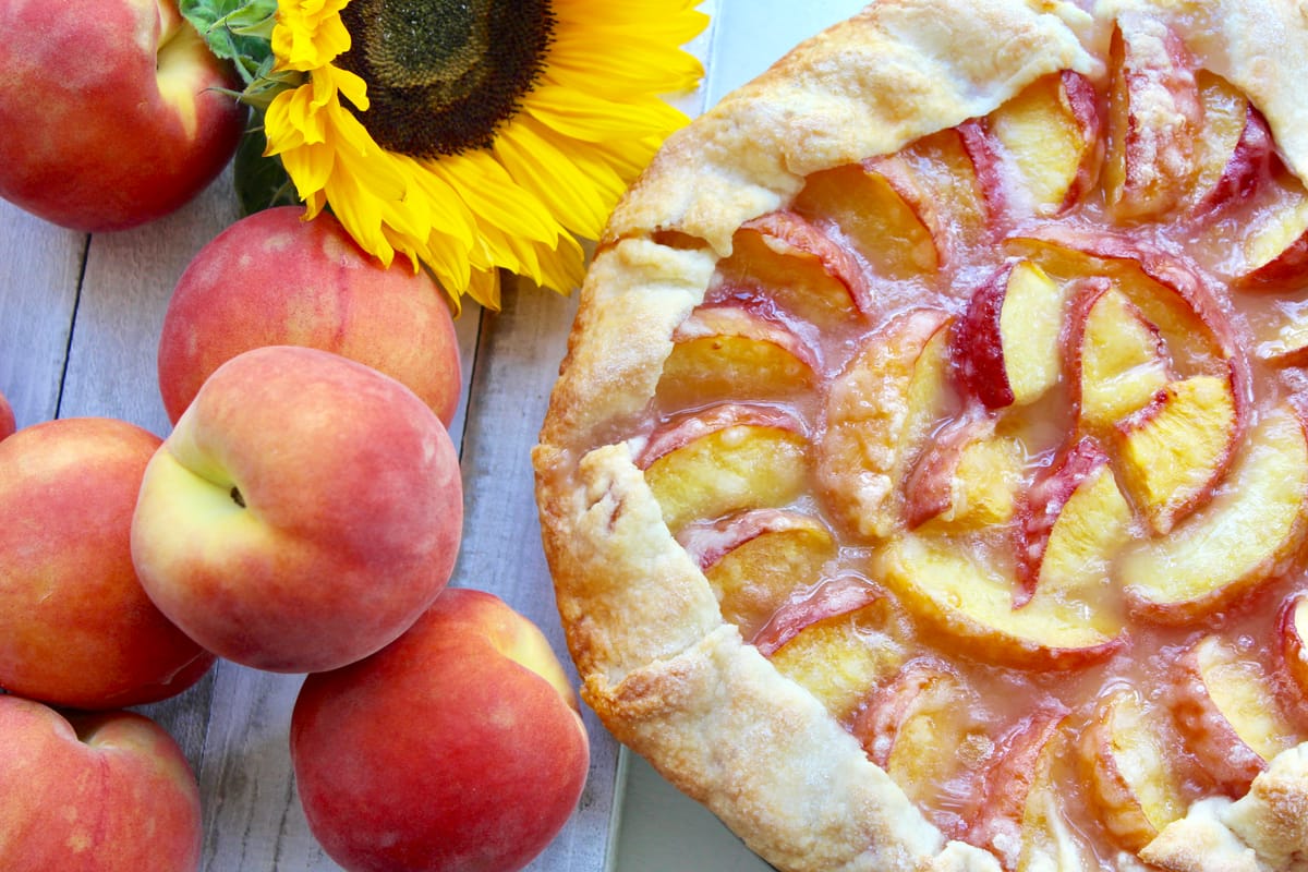 Rustic peach crostata with golden-brown pastry crust folded around fresh peaches on a parchment-lined baking sheet