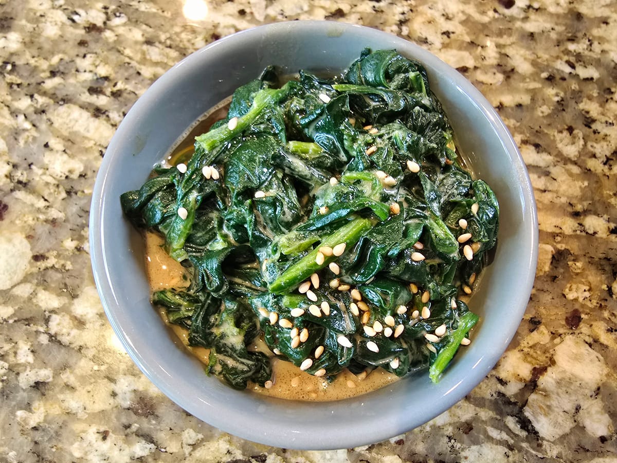 Bowl of vibrant green blanched spinach dressed with nutty sesame sauce, topped with white sesame seeds