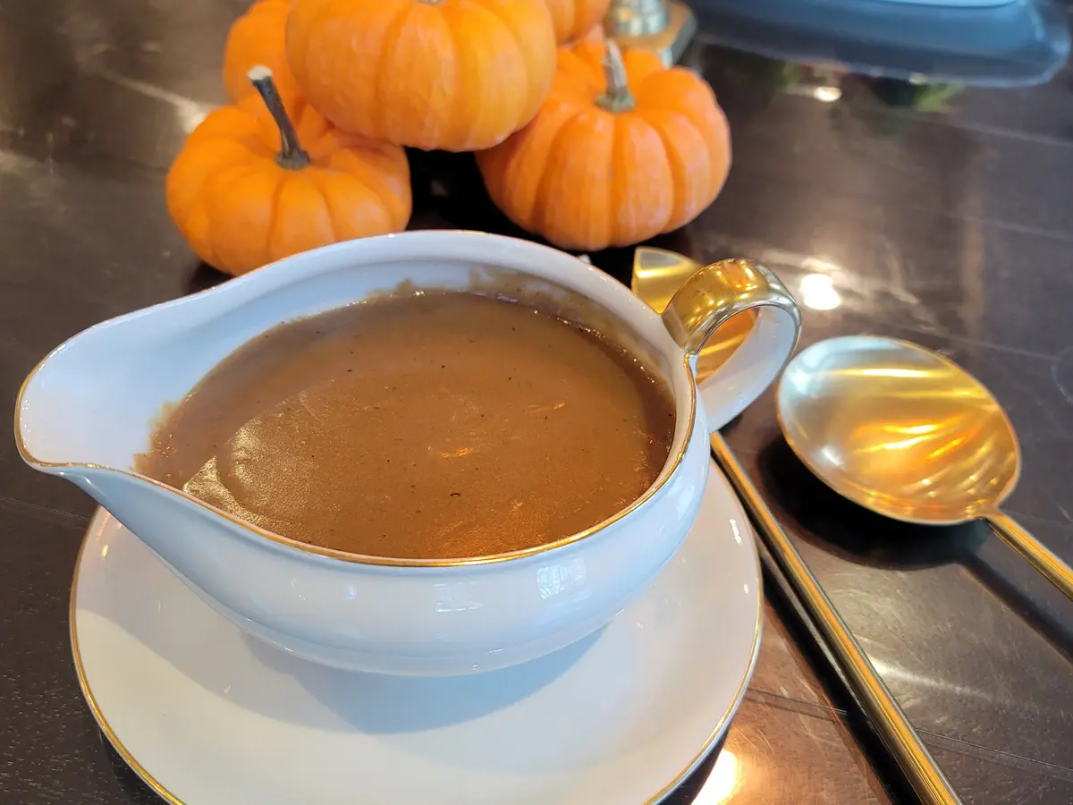 Silky umami-rich gravy in a white bowl with a dark, glossy finish and herbs garnished on top