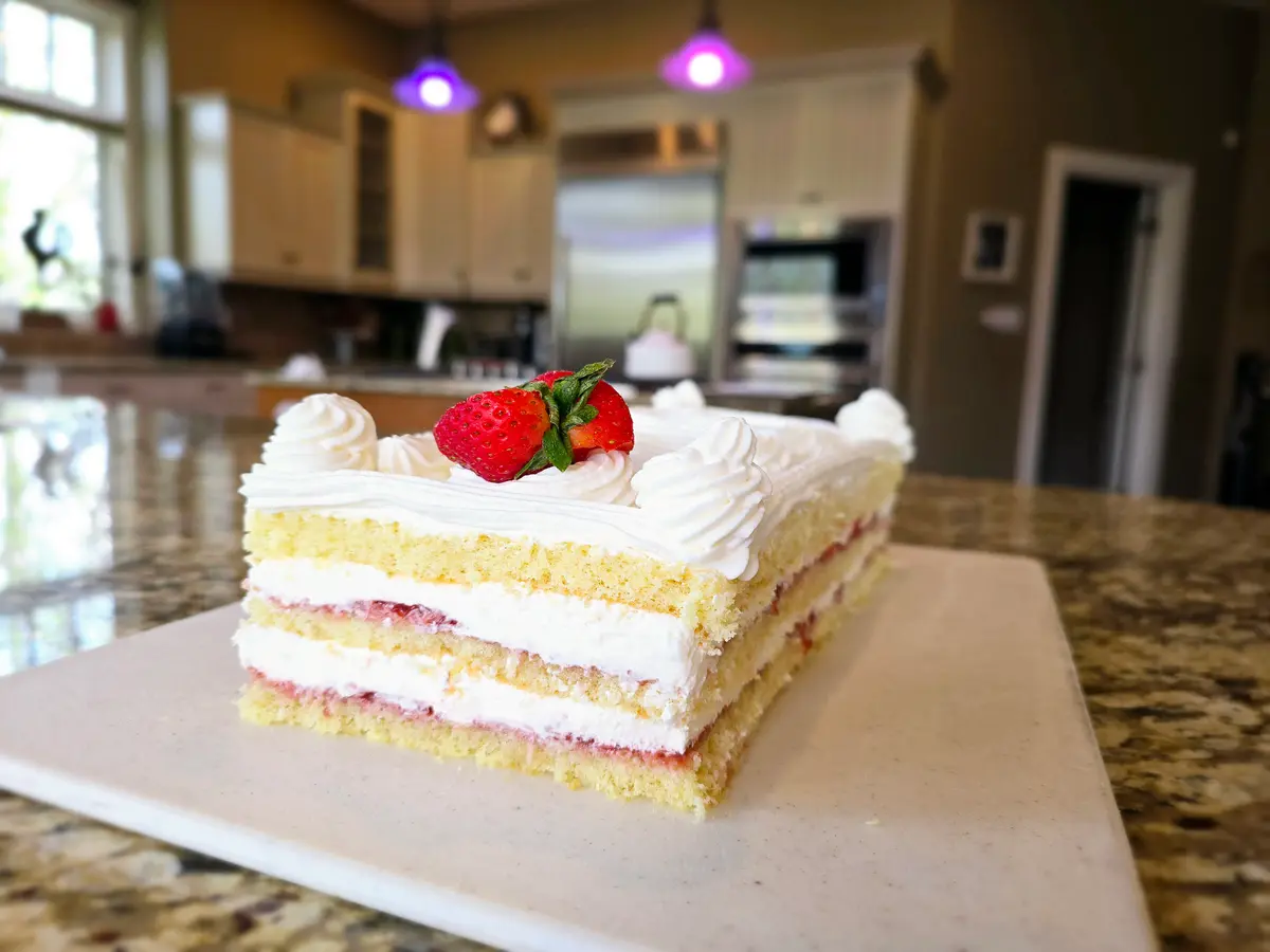 Layered strawberry shortcake bar cake with moist sponge, whipped cream, and fresh strawberry filling on a white plate