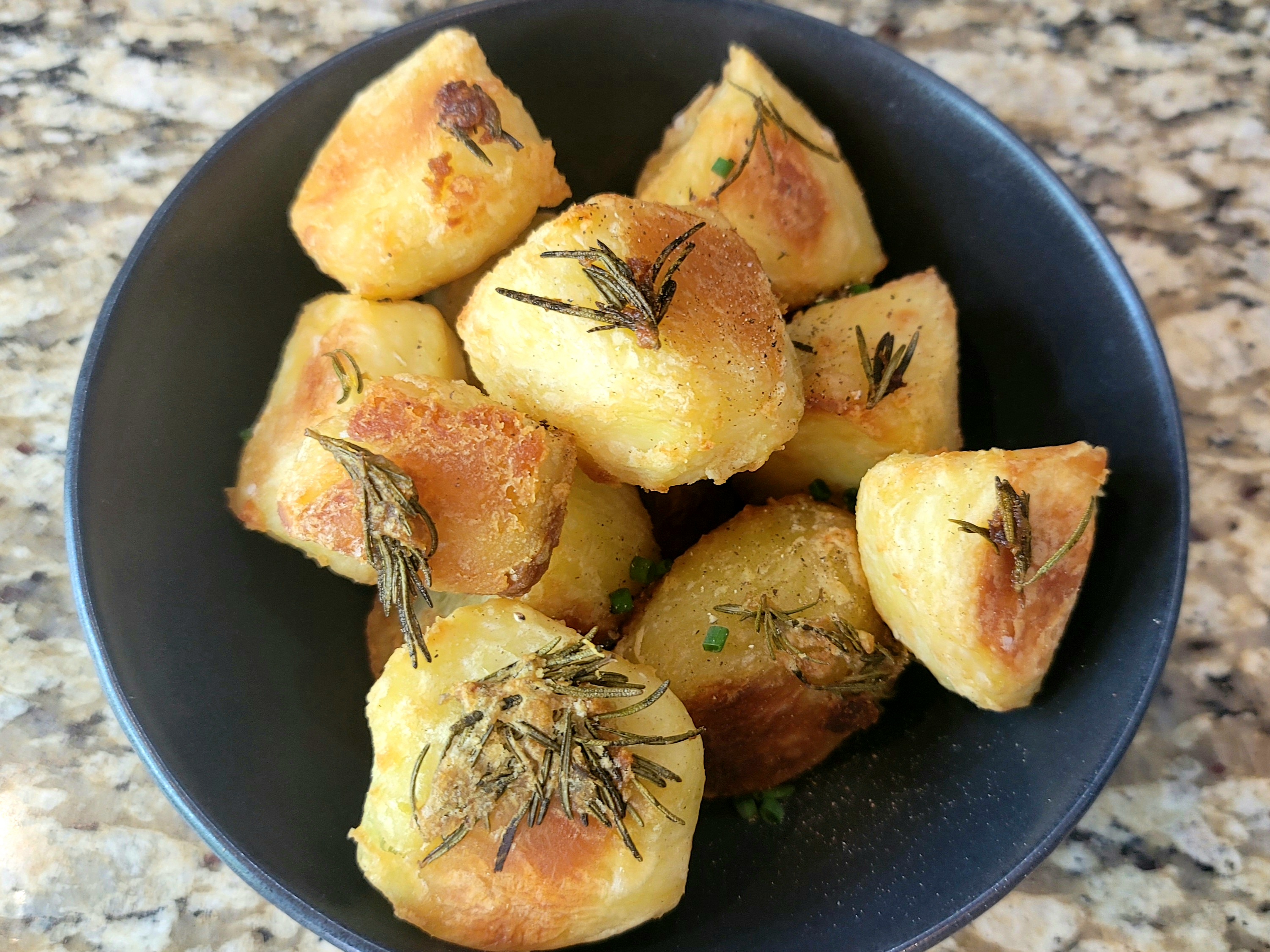 Extra crispy roasted potatoes with golden-brown exterior, fresh rosemary and chives on a white plate