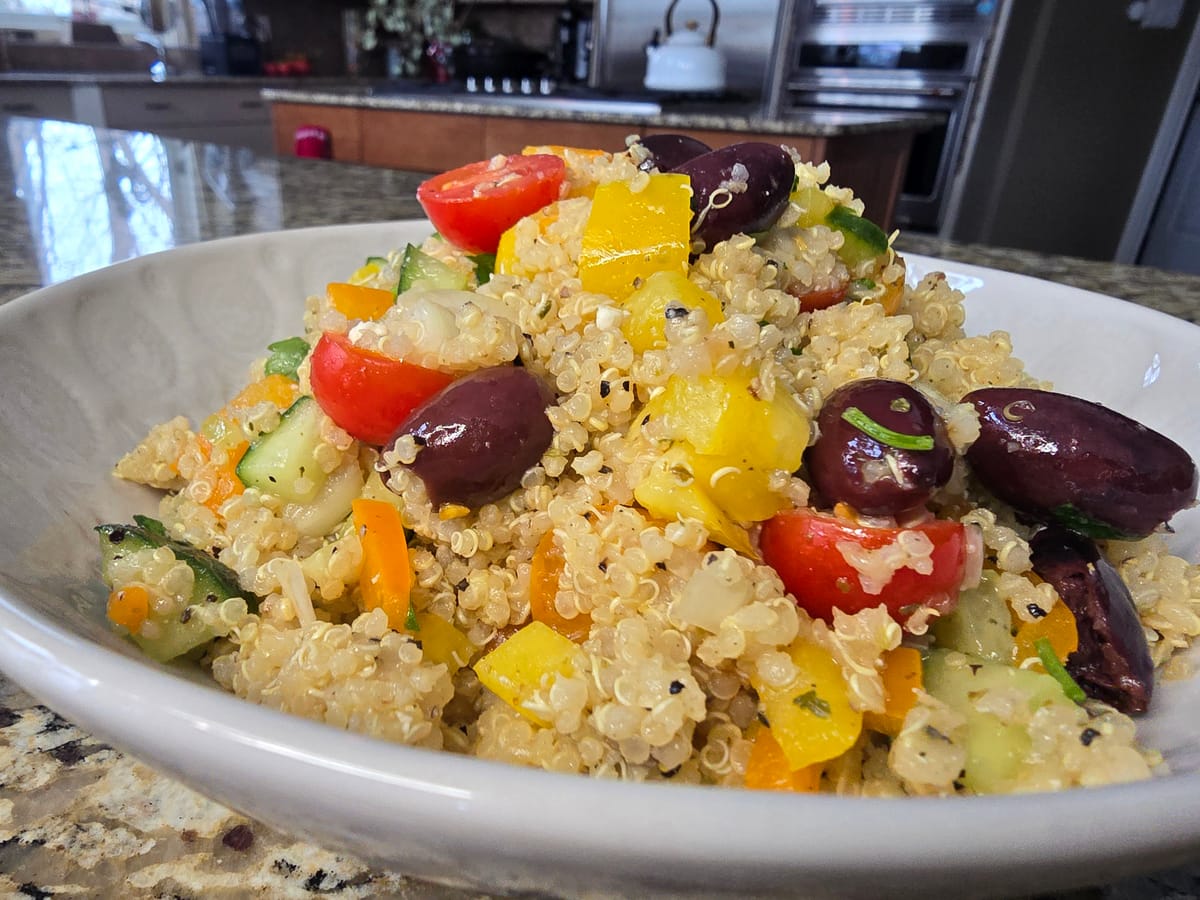 Greek quinoa salad with diced cucumbers, tomatoes, bell peppers, kalamata olives, and crumbled feta cheese on a white plate