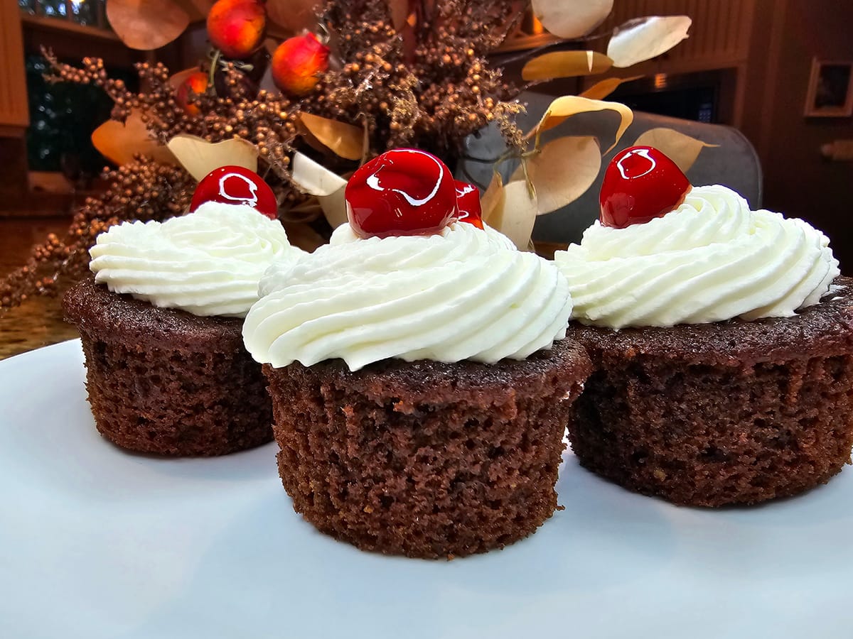 Black Forest Cupcakes topped with mascarpone whipped cream, fresh cherries, and chocolate shavings on a white plate