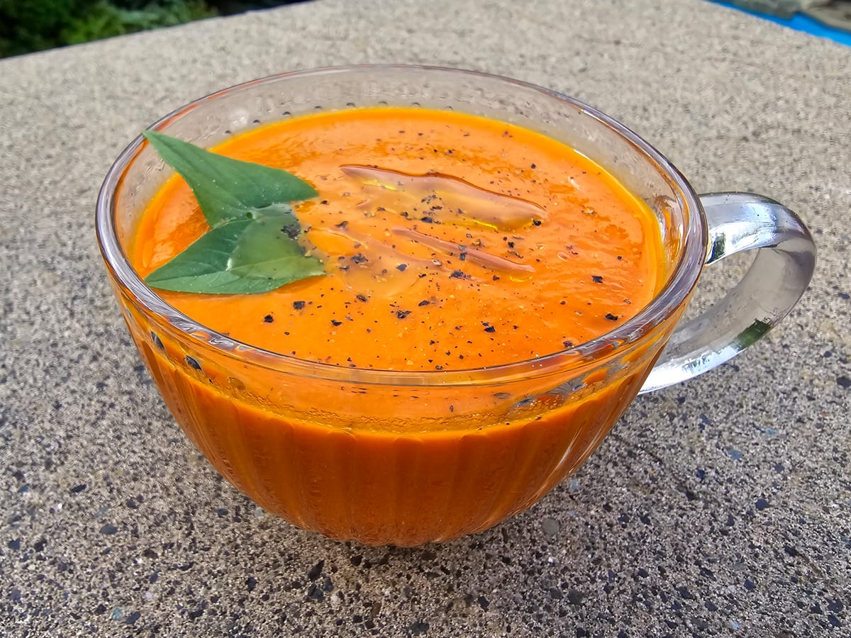 Creamy tomato and roasted red pepper soup in a white bowl with fresh basil garnish and olive oil drizzle