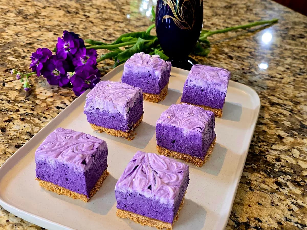 Purple ube cheesecake bars with graham cracker crust on a white plate, showing creamy texture and vibrant purple color