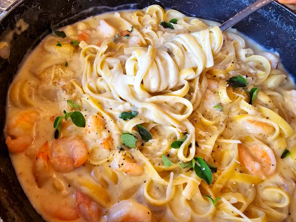Creamy fettuccine alfredo with seafood on a white plate, garnished with fresh parmesan and black pepper