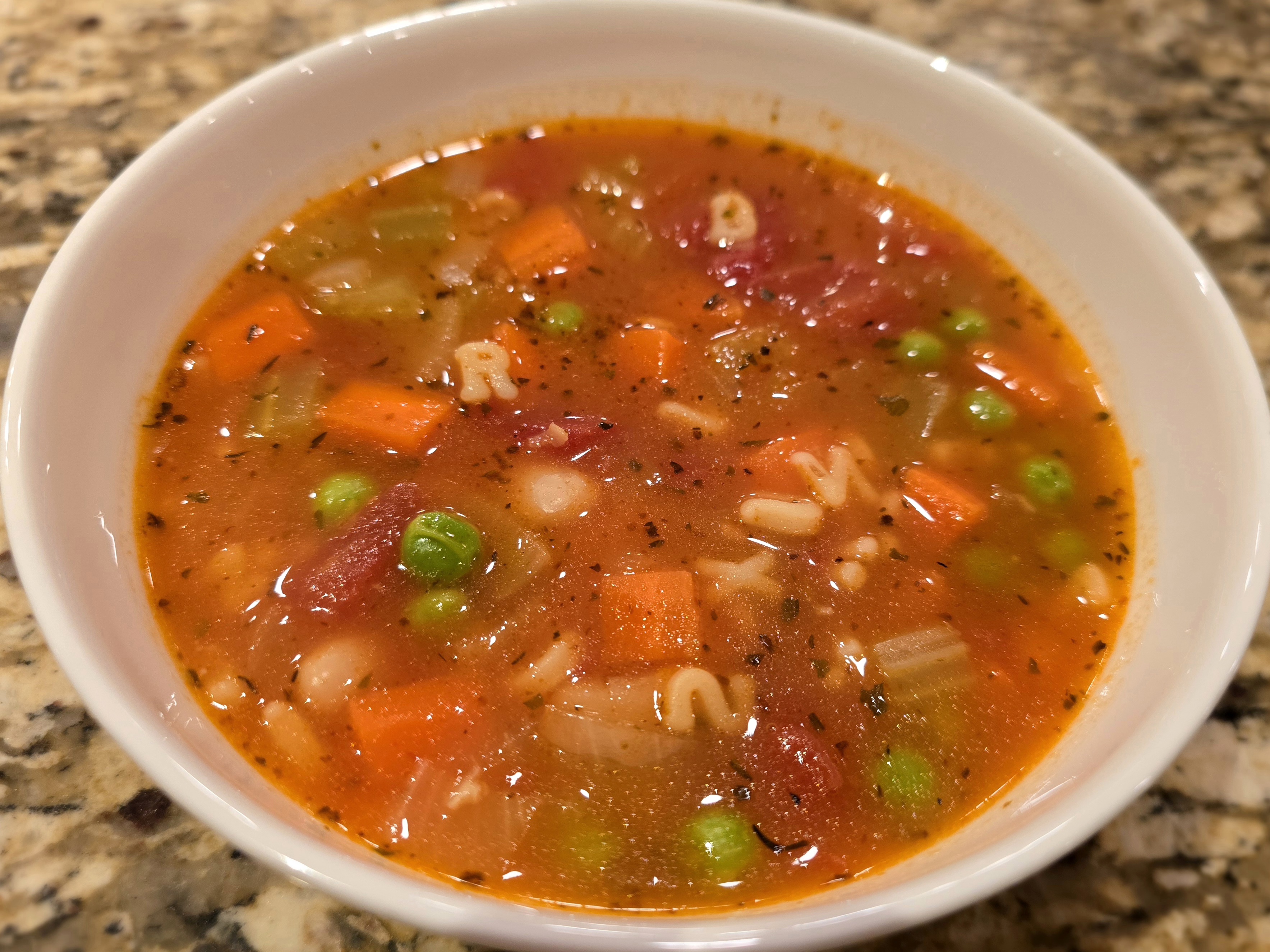 Bowl of cozy alphabet soup with tender vegetables, diced carrots, and tomato broth garnished with fresh herbs