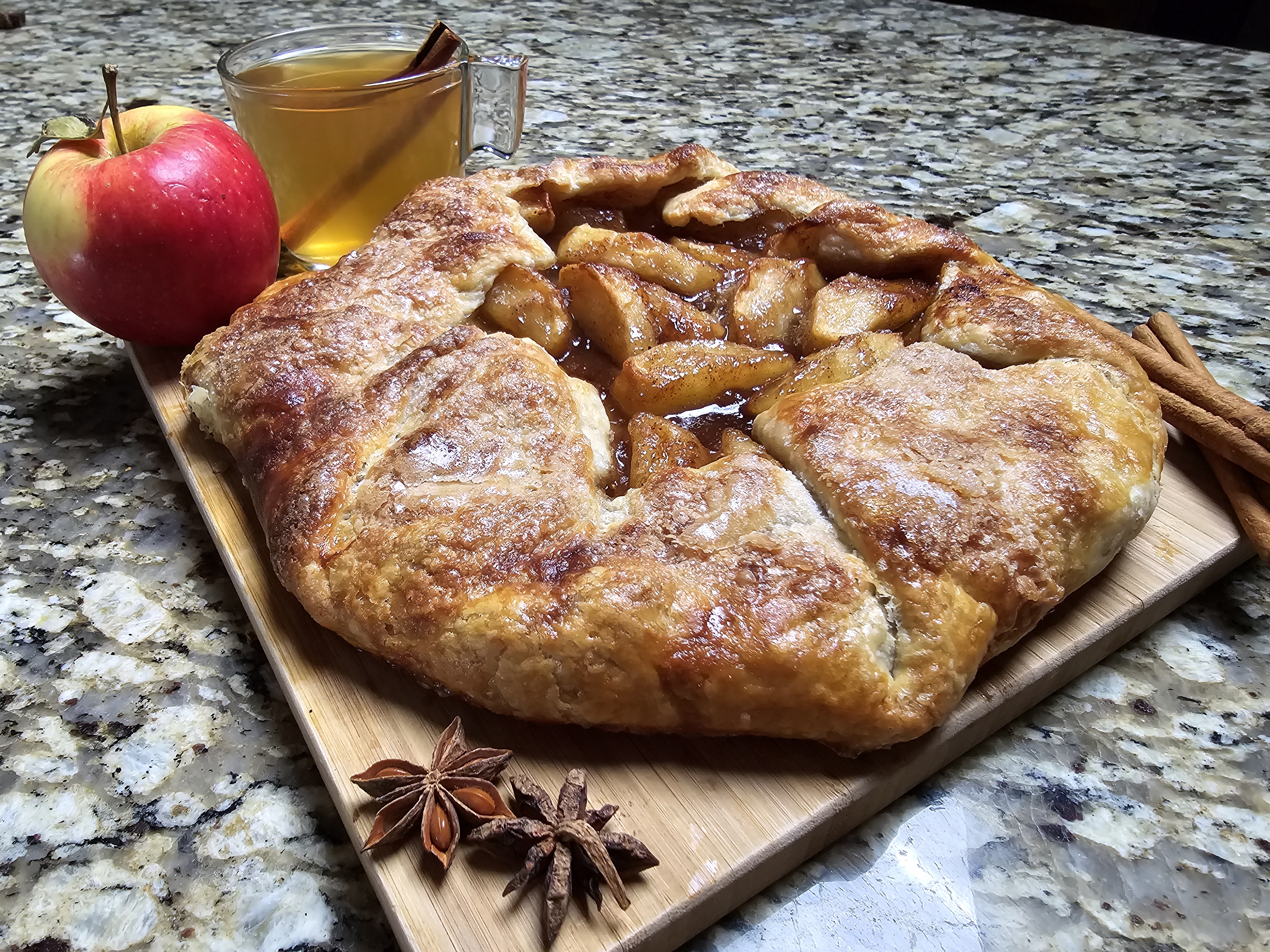 Rustic apple pie crostata on parchment paper with caramelized apple slices arranged in a free-form galette, fluted pastry edges, and a golden-brown crust