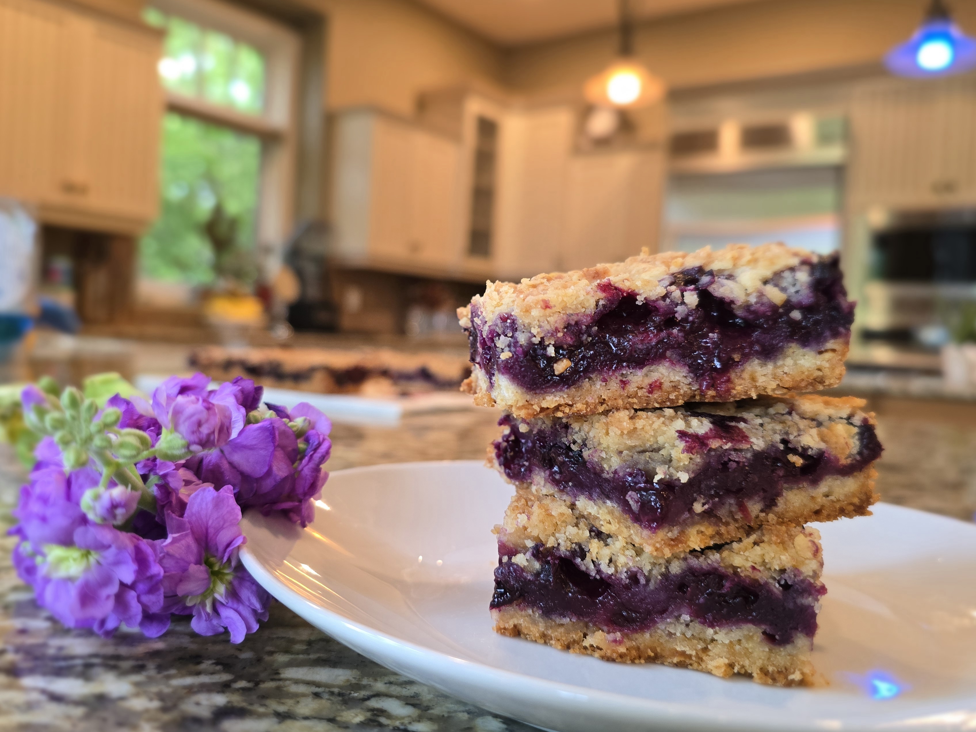 Golden buttery blueberry crumble bars with fresh blueberries, flaky crumb topping, and lemon zest on parchment paper