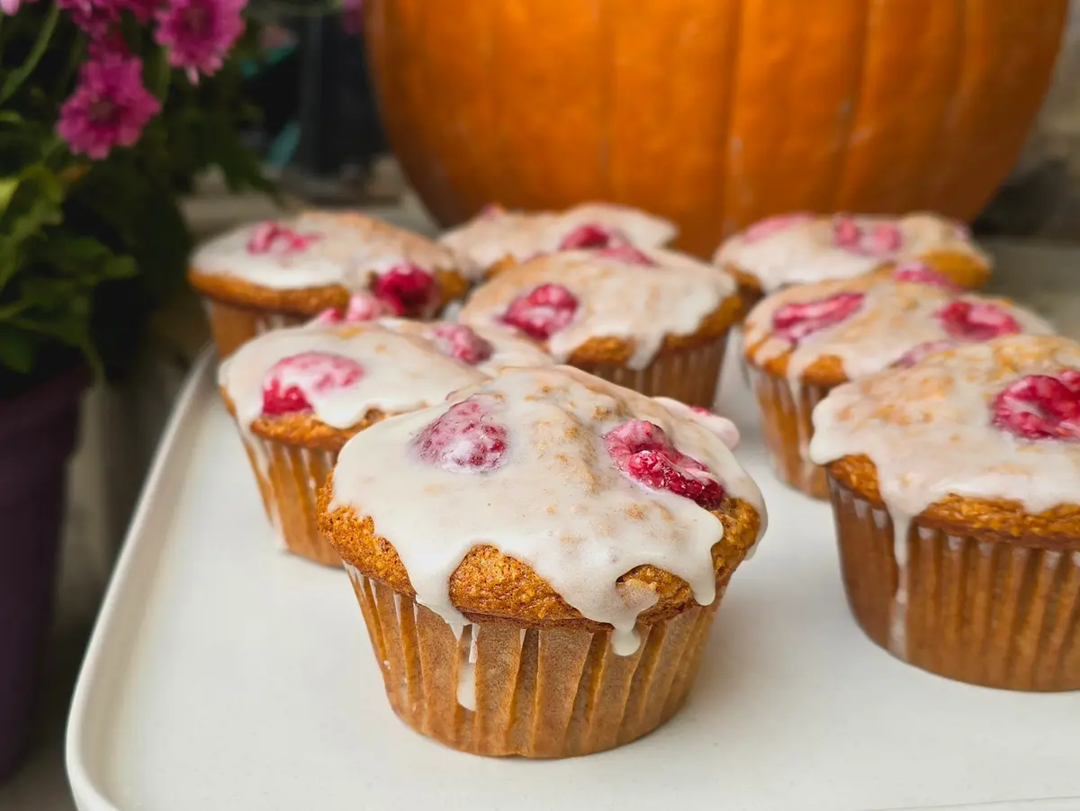 Golden bran raspberry lemon muffins with brown butter honey glaze on a wooden surface with fresh raspberries and lemon slices