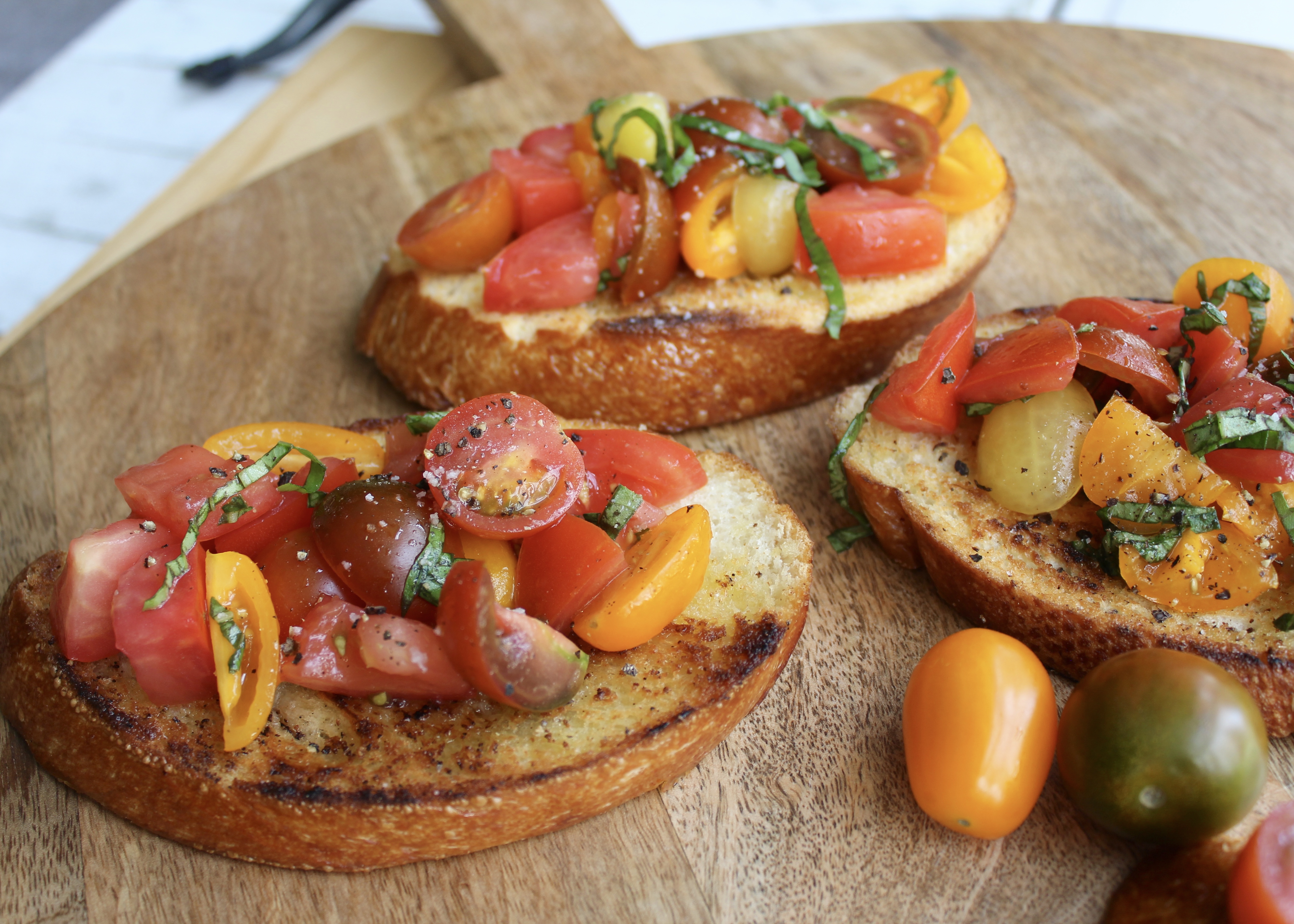 Golden toasted bruschetta slices topped with fresh tomato and basil mixture on a white plate