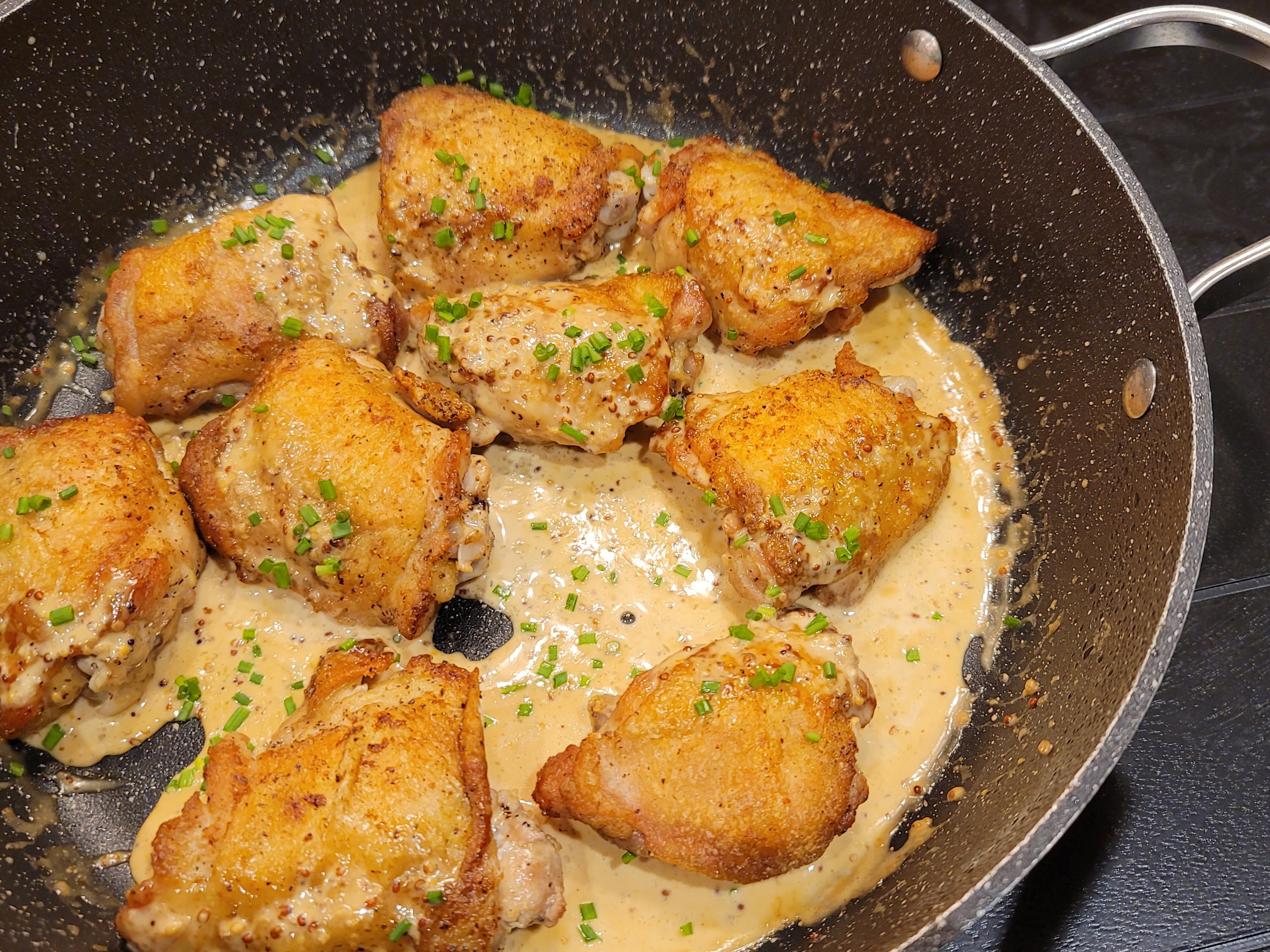 Golden crispy-skinned chicken thighs in creamy mustard sauce on a white plate with fresh herbs garnish