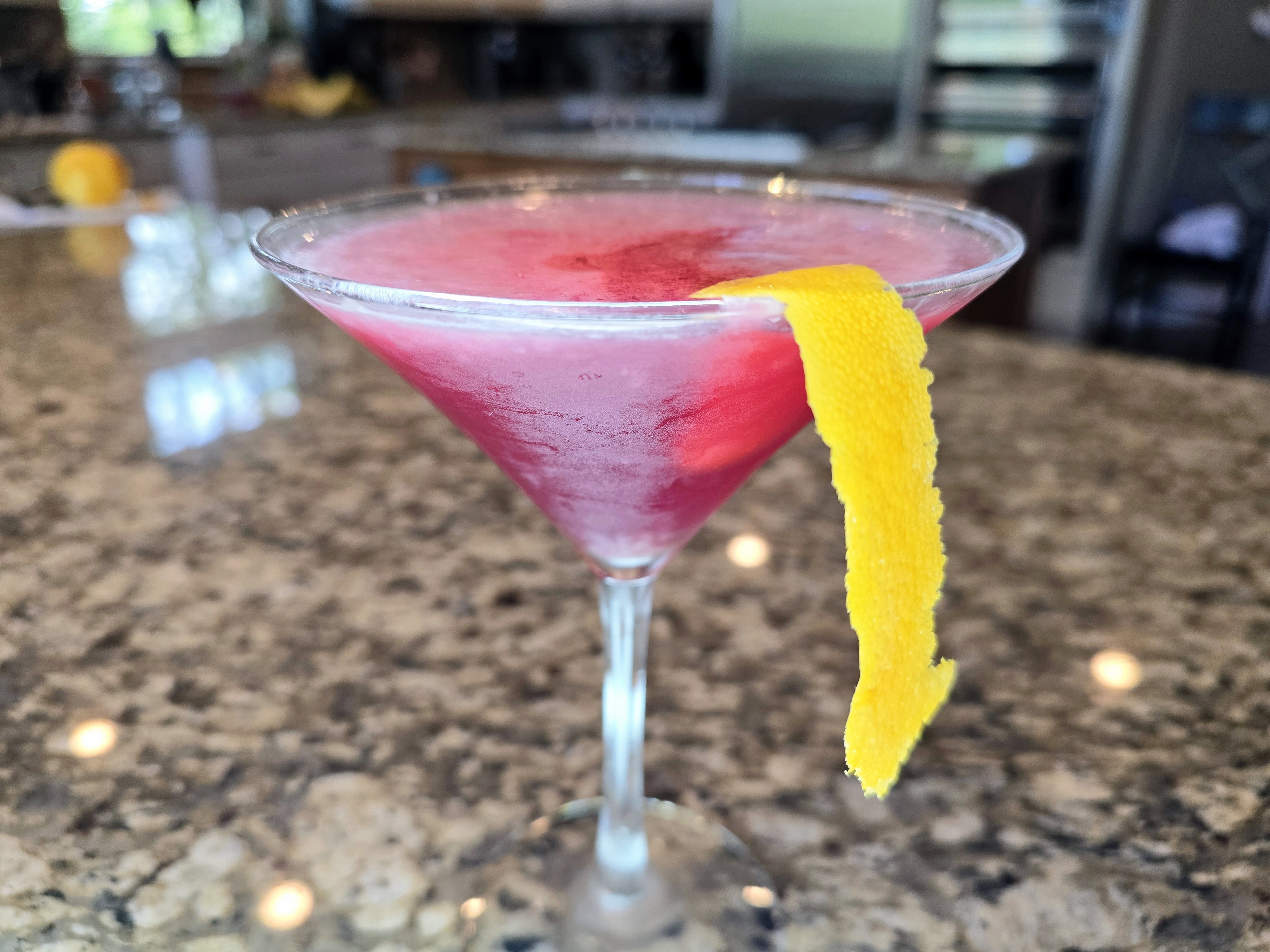 Cosmopolitan cocktail in a coupe glass with cranberry-pink color and orange spiral garnish