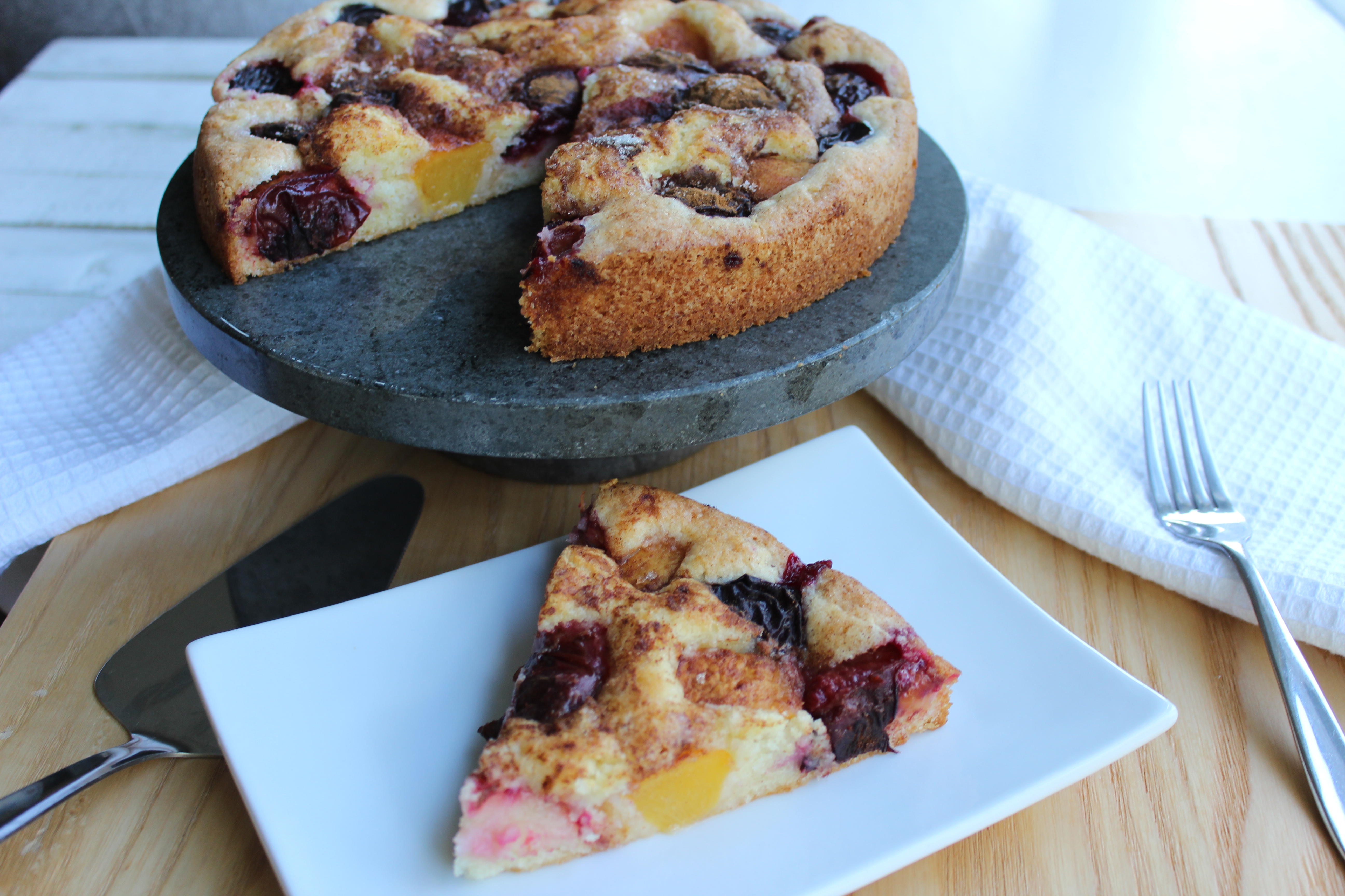 Golden-brown plum torte with fresh purple plums and crumb topping on a round cake pan