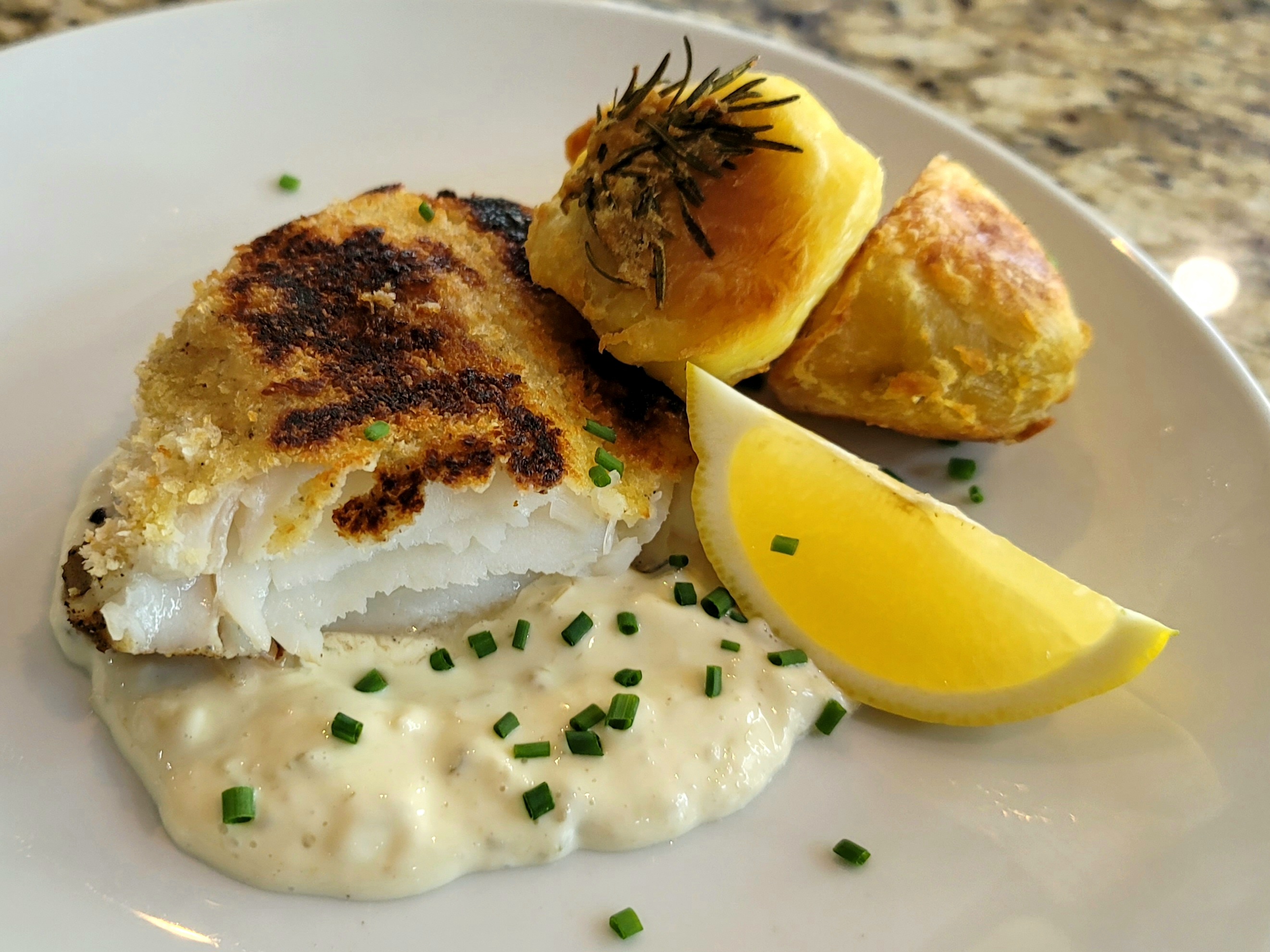 Golden crispy flaky white fish fillet with herb garnish on a white plate, restaurant-style presentation