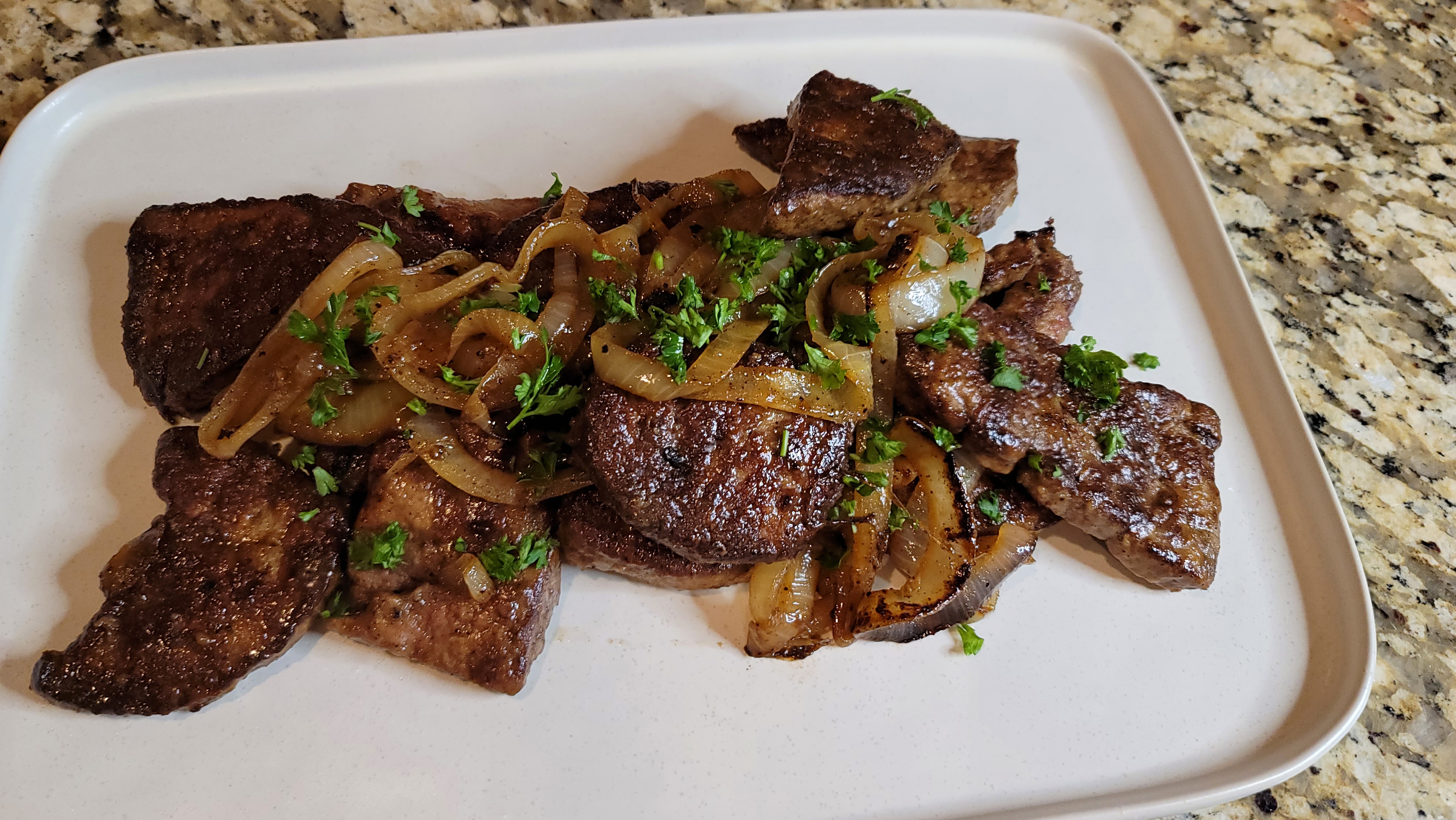 Pan-fried liver and onions on a white plate with golden caramelized onions and fresh herbs
