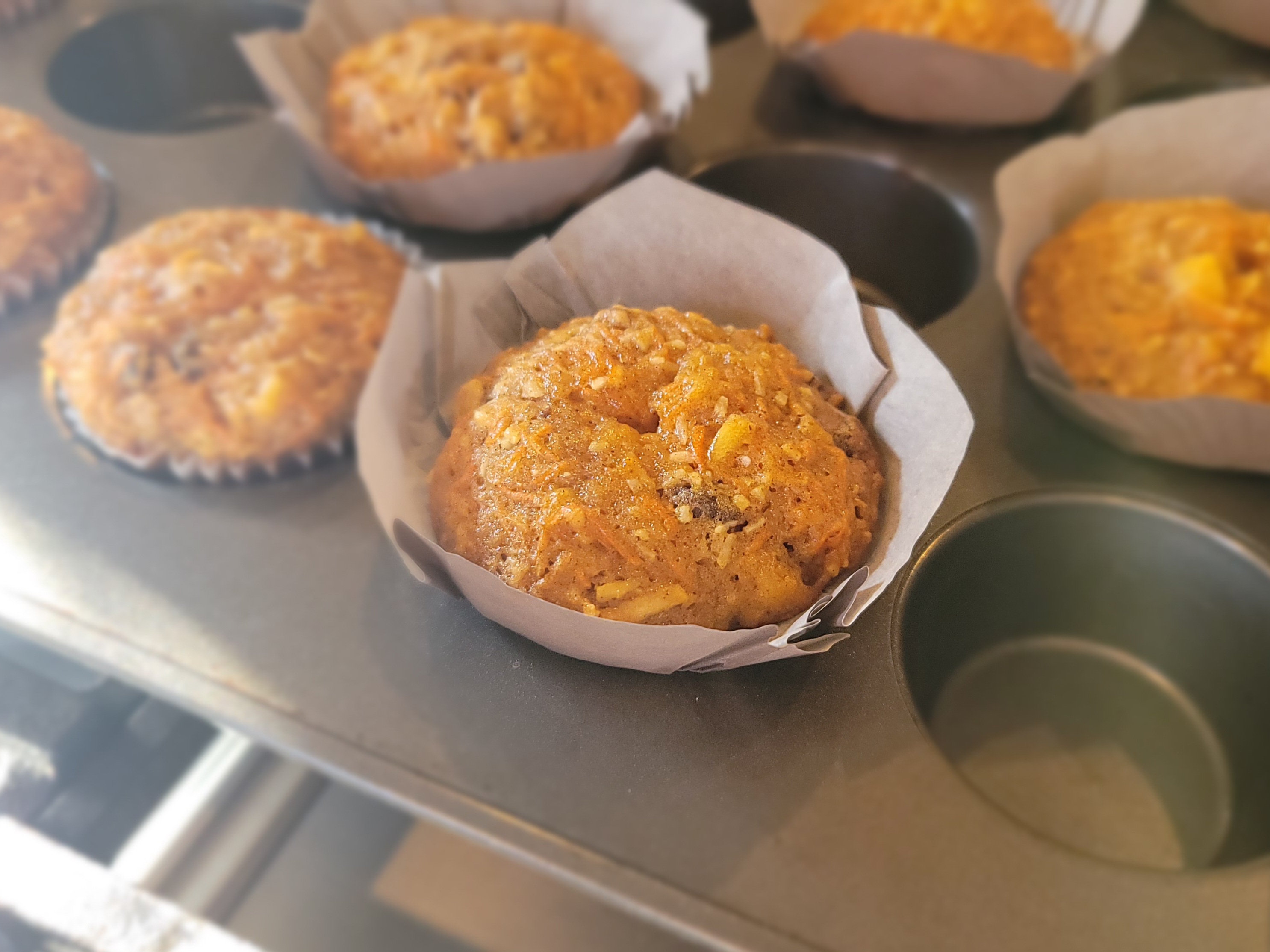 Golden-brown morning glory muffins in a muffin tin, studded with shredded carrots, apples, and walnuts, showing moist texture