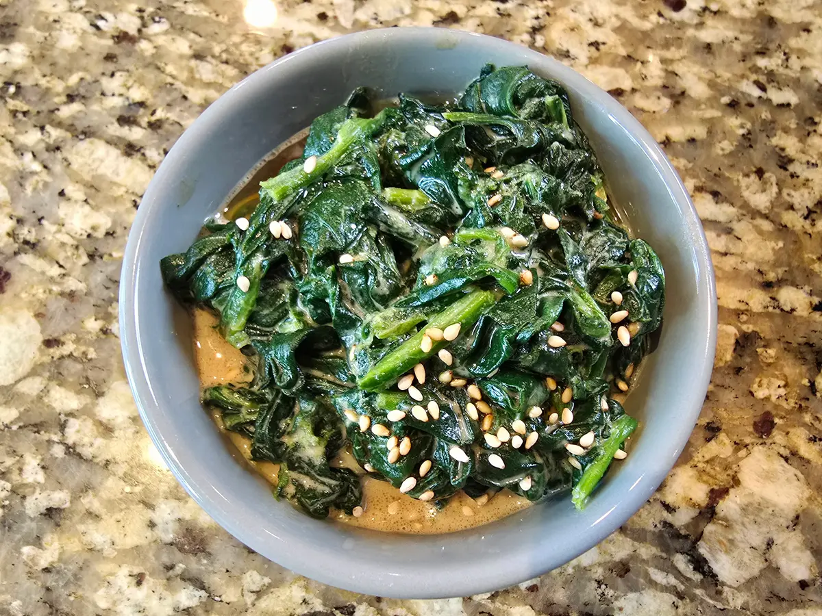 Bowl of vibrant green blanched spinach dressed with nutty sesame sauce, topped with white sesame seeds