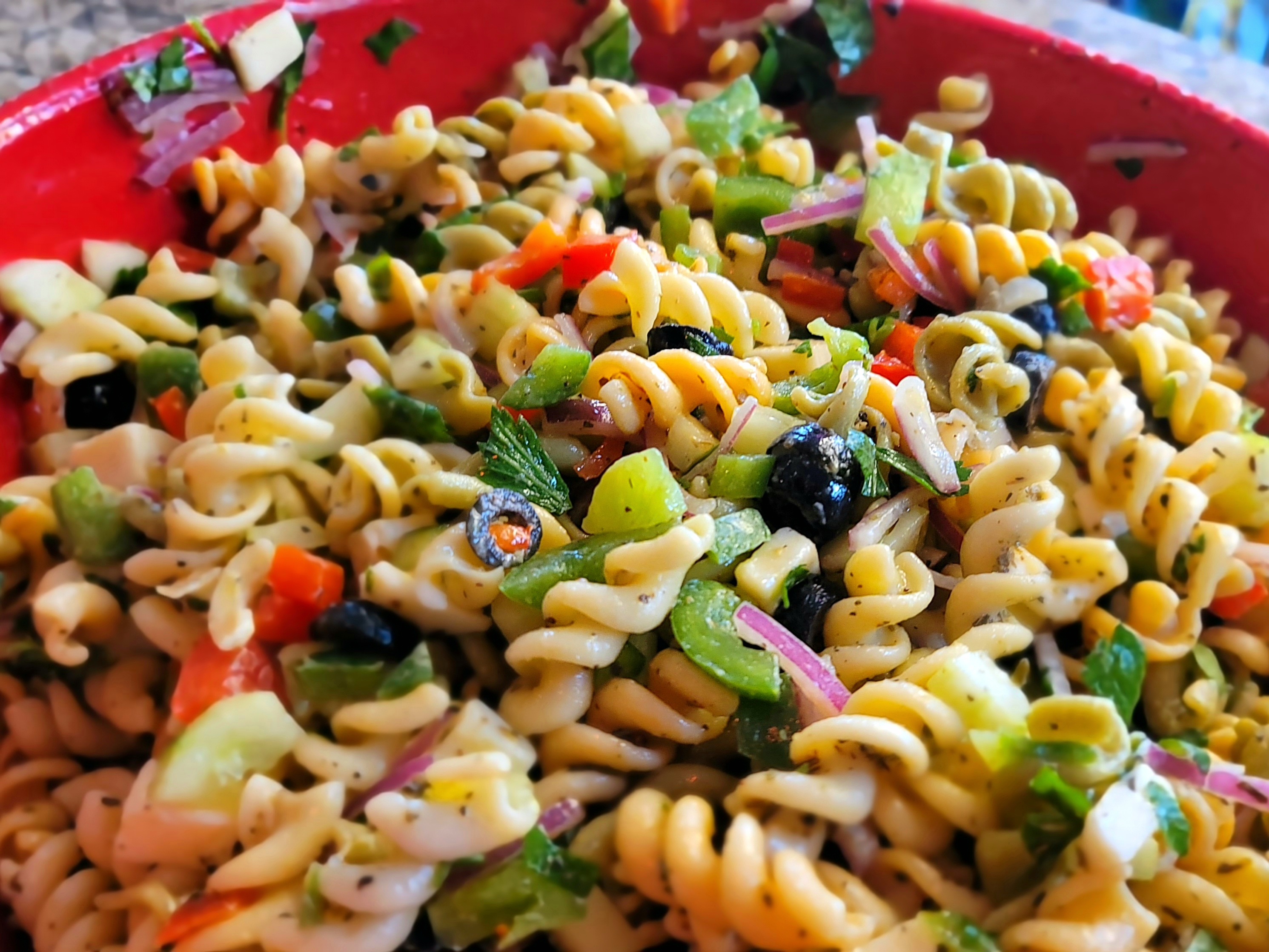 Colorful pasta salad with rotini, cherry tomatoes, bell peppers, cucumber, olives, and provolone cheese in a large white bowl
